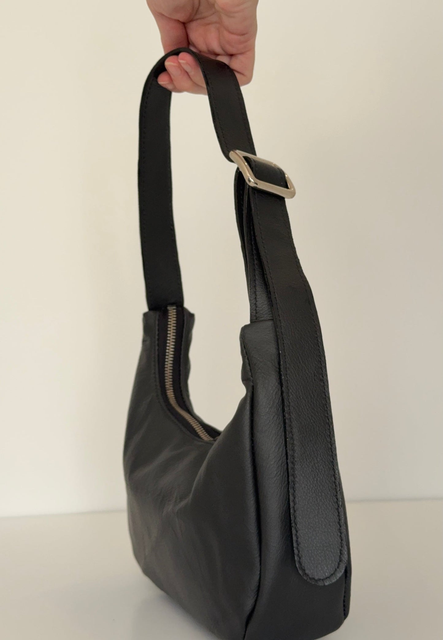 Black leather baguette shaped handbag held by a hand against a plain background