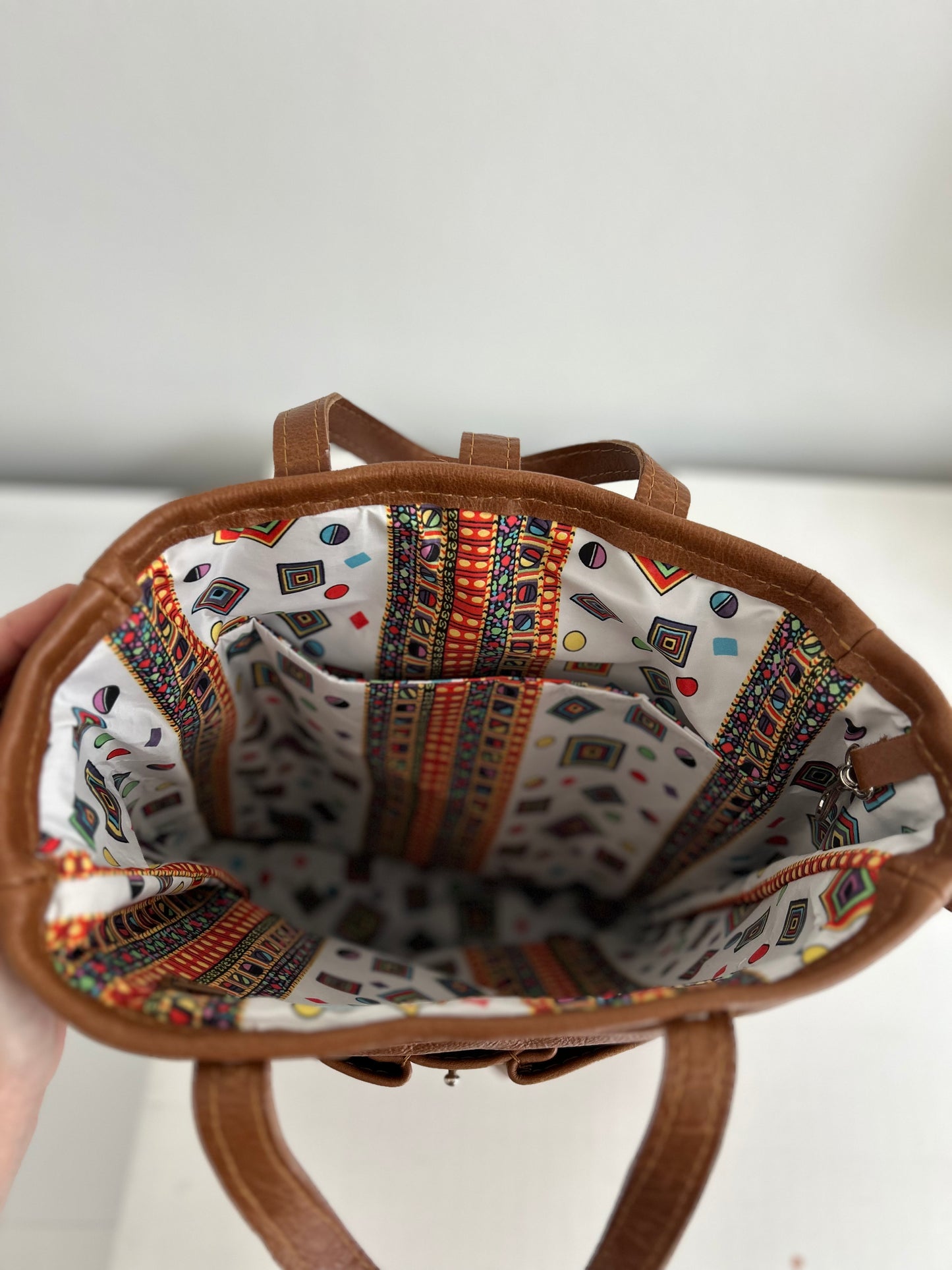 Dark tan leather tote with 2 external pockets and an internal space for a lap top. A long strap for over the shoulder or cross body carrying. It has 2 small handles. The bag is lined in a bright water-resistant fabric