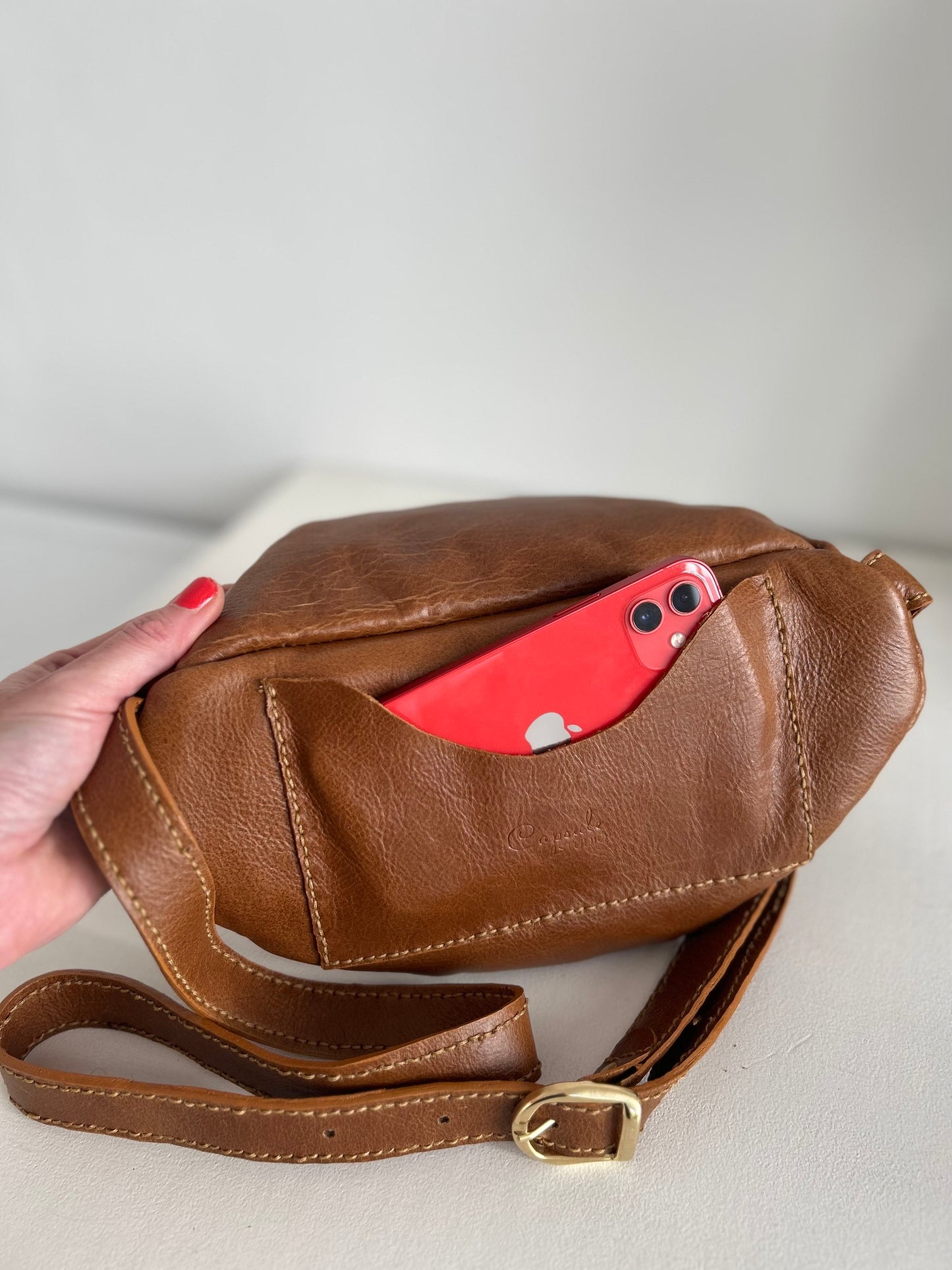 Dark tan leather moon bag with adjustable strap. There is a rear pocket for your cell phone for easy accessibility.