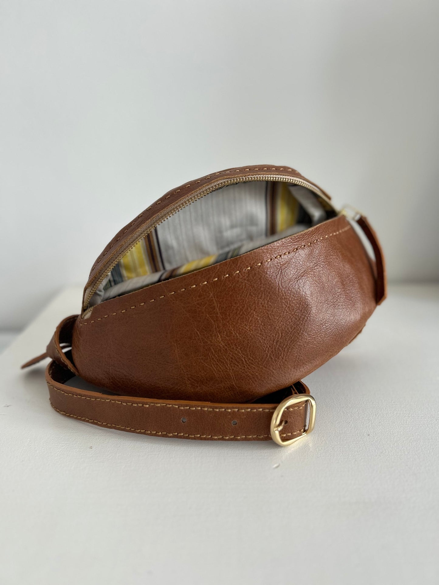 Dark tan leather moon bag with adjustable strap. Lining is a fun brown, yellow and cream stripe.