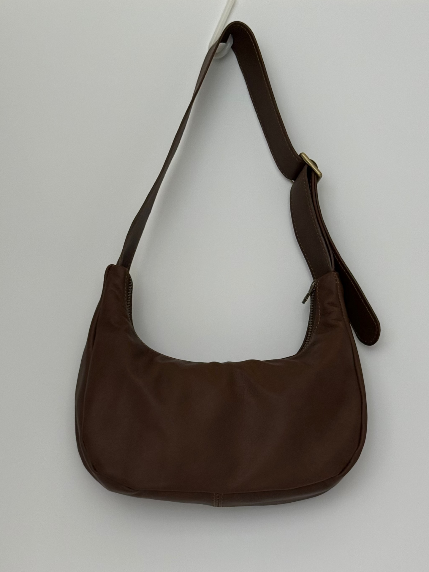 Brown leather handbag with antique brass zip and slider hanging on a white wall