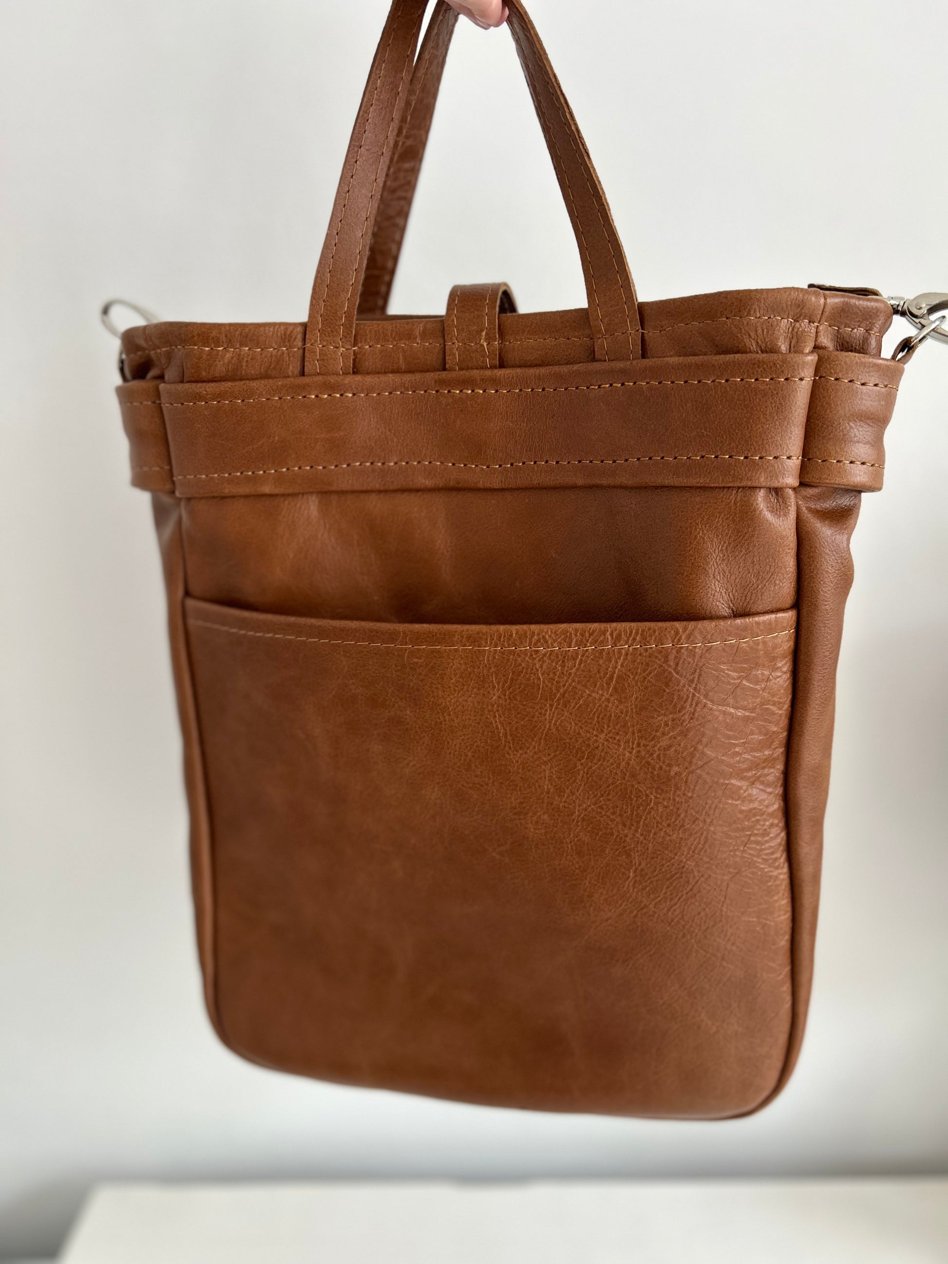 Dark tan leather tote with 2 external pockets and an internal space for a lap top. A long strap for over the shoulder or cross body carrying. It has 2 small handles