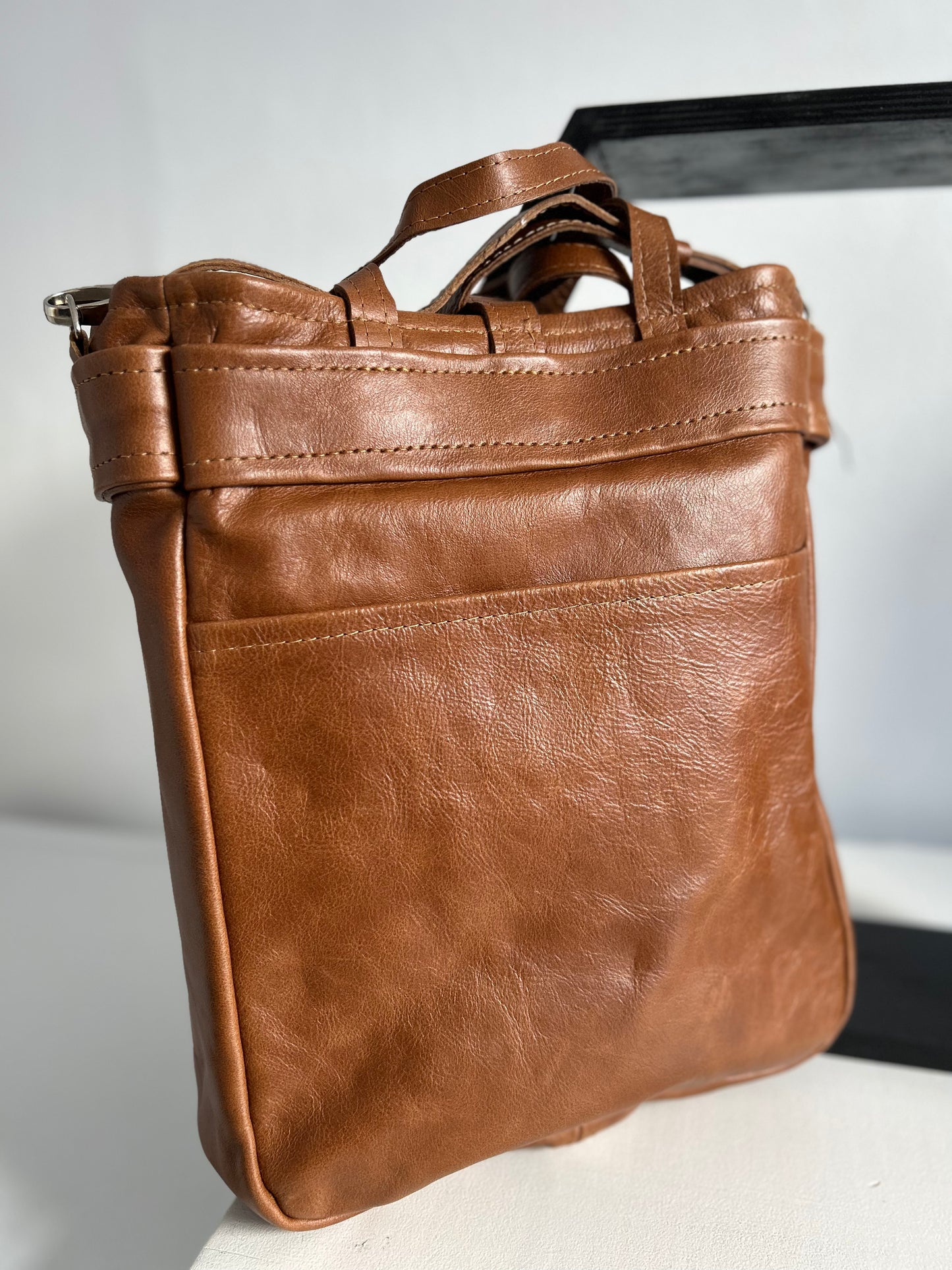 Dark tan leather tote with 2 external pockets and an internal space for a lap top. A long strap for over the shoulder or cross body carrying. It has 2 small handles