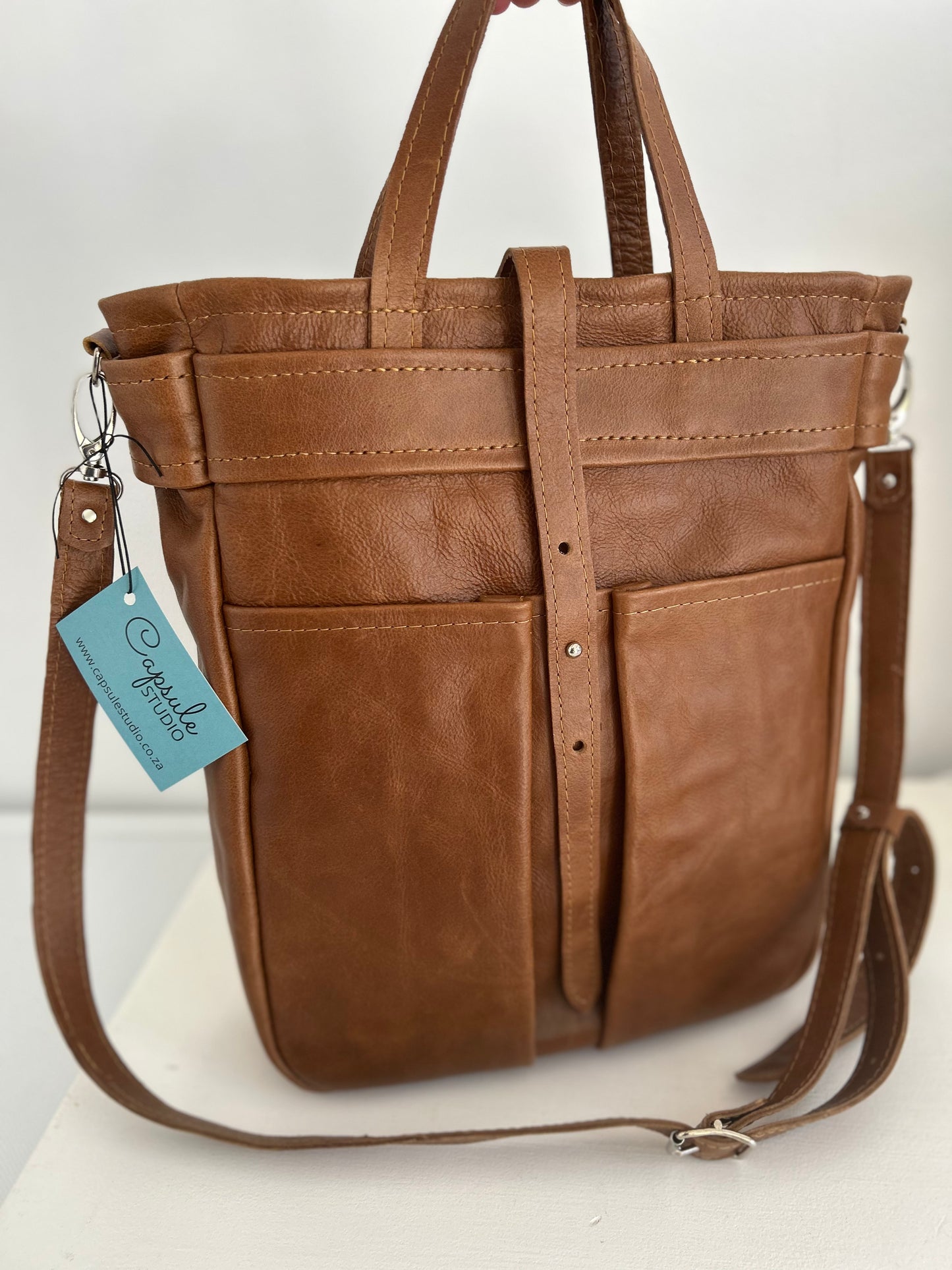 Dark tan leather tote with 2 external pockets and an internal space for a lap top. A long strap for over the shoulder or cross body carrying.  It has 2 small handles. 